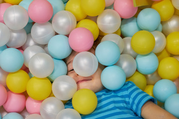child of three years old is playing in a ball pool. boy smiling spends fun time in the children's room