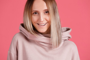Fototapeta premium Close-up - portrait of a beautiful young female student positively smiling and looking into the camera against a pink background