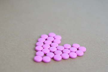 pink pills laid out in shape of a heart on brown background. coloured drugs. concept - heart disease, heart disorders and drugs, cardiology, valentines, love,