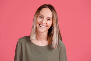 Fototapeta premium Portrait of young excited smiling woman in green T-shirt. Funny happy girl with ombre on pink background looking at camera. People expression, portrait happy girl