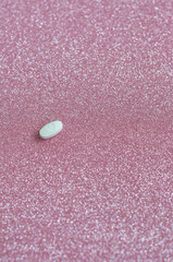 White pill with heart shape, love shape medicine isolated on glitter pink background.