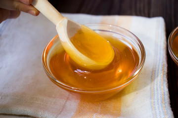 Honey dripping from honey dipper on yellow background. Thick honey dipping from the wooden honey...