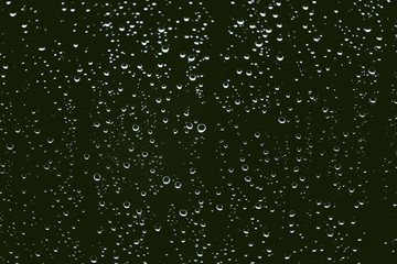 Dirty window glass with drops of rain. Atmospheric green background with raindrops. Droplets and stains close up. Detailed transparent texture in macro with copy space. Rainy weather.