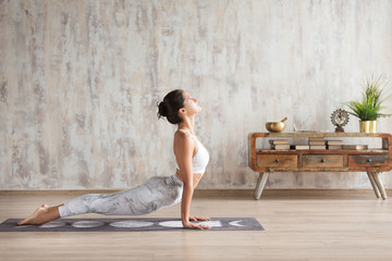 Young indian girl doing yoga fitness exercise indoor. Wellness concept. Calmness and relax. Yogi Instructor doing Urdhva mukha shvanasana exercise, upward facing dog pose, working out, home interior - obrazy, fototapety, plakaty