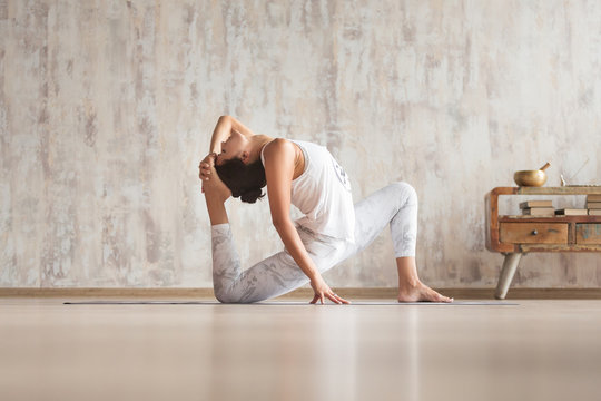 Charming young beautiful woman yoga instructor doing yoga asana for back and leg joints standing on the floor against the background of a concrete wall and vintage console