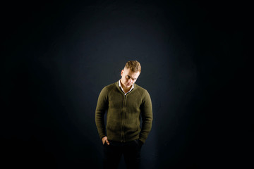Young handsome man wearing green pullover standing on the gray background and posing at the studio