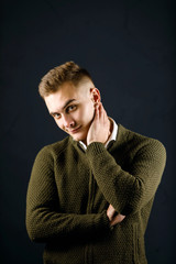 Portrait of young handsome man wearing green pullover standing on the gray background and holding his neck at the studio