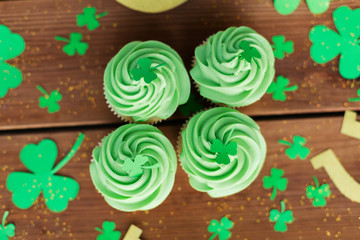 st patricks day, food and holidays concept - green cupcakes and shamrock on wooden table top view