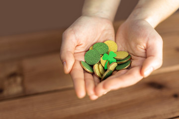 fortune, luck and st patricks day concept - hands holding golden coins and shamrock leaf on wooden background