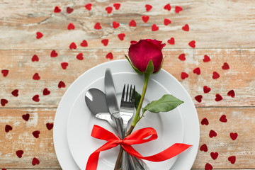 valentines day and romantic dinner concept - close up of red rose flower on set of dishes with...