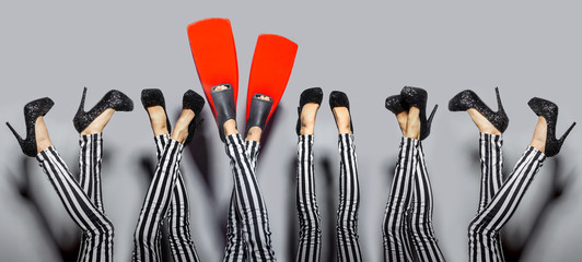 Standing out from others concept. Female sexy legs wearing high heels and one woman wears red flippers isolated over gray background