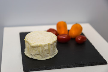 Tomino Cheese on Black Tablecloth decorated with Red and Orange Tomatoes