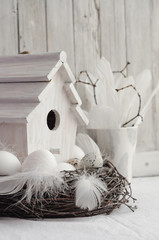 Easter. White eggs on wooden table with feathers, branches and birdhouse