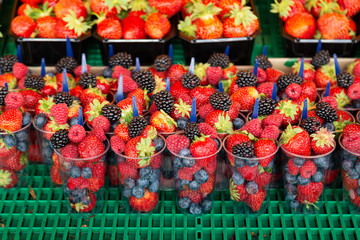 Fresh berries on sale at the market. Close up of plastic cups filled with assorted summer berries - blueberries, strawberries, raspberry and blackberries on a market stall. 