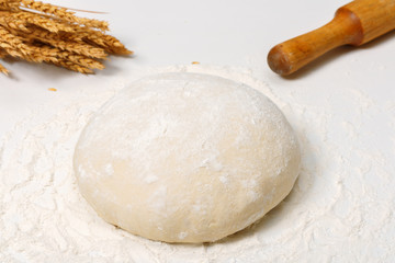 Fototapeta na wymiar Raw fresh dough in the flour and ears of wheat on a white backgr