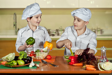 The boys in the cooks costumes cut the salad in the kitchen. Children prepare healthy food. Friendly cooperation of cooks.
