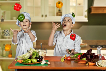 The boys in the cooks costumes cut the salad in the kitchen. Children prepare healthy food. Friendly cooperation of cooks. Juggle with vegetables.