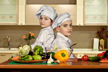 The boys in the cooks costumes cut the salad in the kitchen. Children prepare healthy food. Friendly cooperation of cooks.