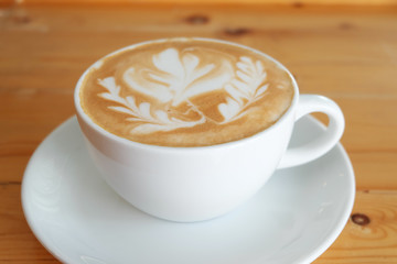 A white cup of hot latte coffee with latte art,on the wooden dinning table at the cafe