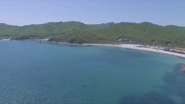 Aerial shot moving along the coastline of deep blue sea along a dramatic cliff edge on sunny day