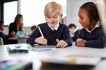 A girl and a boy using a tablet computer and stylus in a primary school class, front view, selective focus