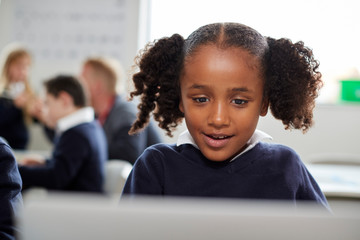 Young black schoolgirl using a laptop computer sitting at desk in a primary school classroom, front...