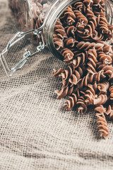 fusilli pasta - raw whole-grain Italian pasta of dark color on a linen cloth in the kitchen - vertical