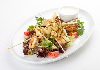 Squid grilled on skewers, with salad and sauce. On white background