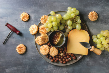 Obraz na płótnie Canvas Wine snack. Cheese, grapes, nuts, cheese crackers cookies, honeycombs with knife over dark texture background. Flat lay, space