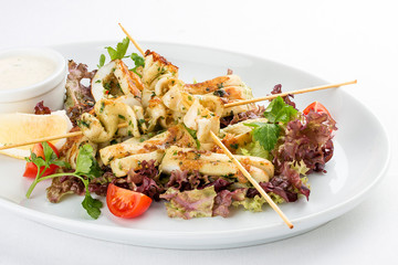 Squid grilled on skewers, with salad and sauce. On white background