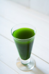 glass of green vegetable beverage on white wooden background