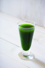 glass of green vegetable beverage on white wooden background