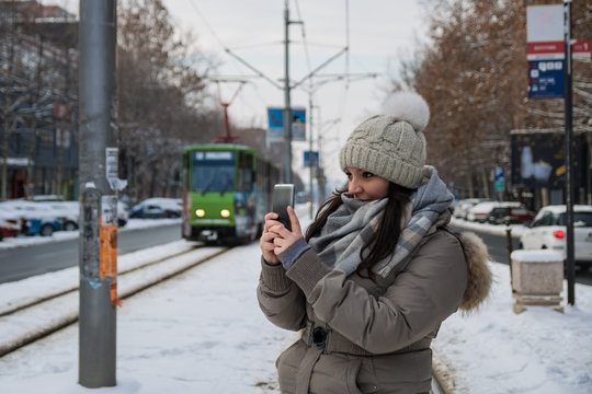 Beautiful women holding mobile phone and waiting for a bus on snow winter day
