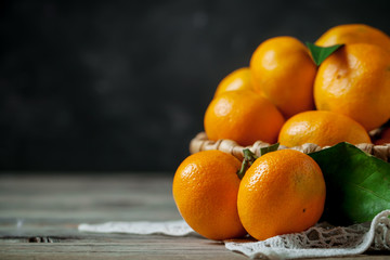 Tangerines with leaves in basket on rustic wooden background.