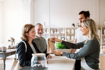 Senior couple buying groceries in zero waste shop, sales assistants serving them.