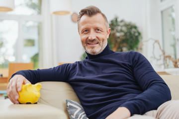 Relaxed mature man on home with piggy bank