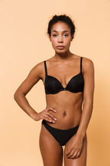 Fototapeta premium Beauty portrait of elegant woman wearing black lingerie, standing isolated over beige background