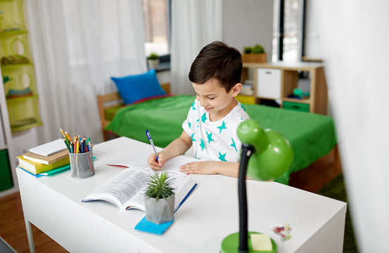 education, childhood and people concept - happy student boy with book writing to notebook at home