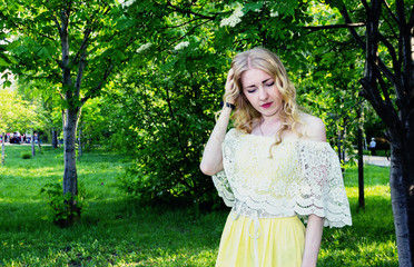 Sad blonde girl in white blouse and yellow dress in city Park.