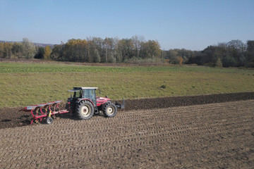 Obraz premium A farmer on a red tractor with a seeder sows grain in plowed land in a private field in the village area. Mechanization of spring field work. Farmer's everyday life. Processing of land. The agrarian.