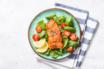 Baked salmon fish fillet with fresh salad top view on white.