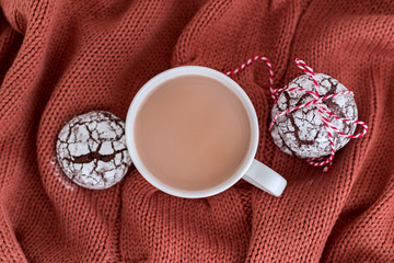 Cup of coffee with milk and chocolate cookies on warm knitted coral blanket.