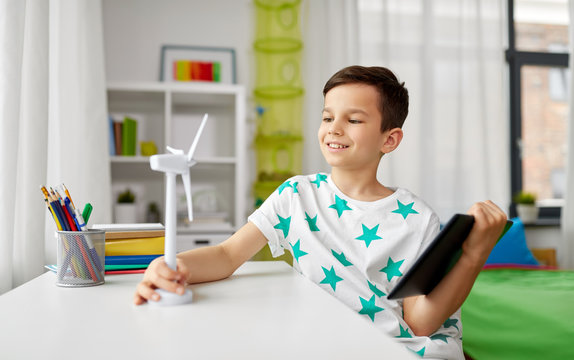 ecology, technology and energy saving concept - smiling boy with tablet pc computer, toy model of wind turbine at home