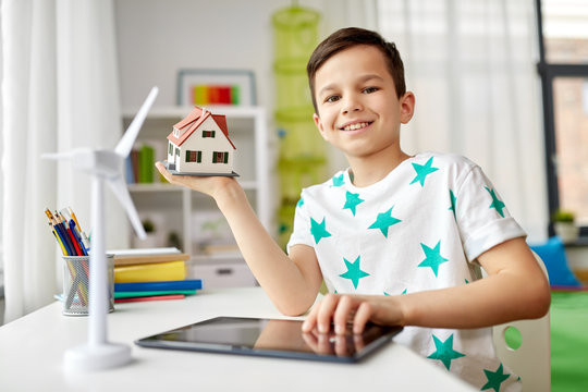 ecology, technology and energy saving concept - smiling boy with tablet pc computer, toy house model and wind turbine at home