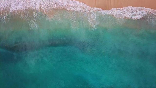 Beach scene, view from above - waves of turquoise ocean waters crashing on yellow sand. 4k footage.