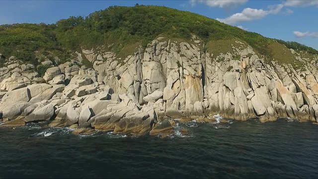 Aerial shot moving along the coastline of deep blue sea along a dramatic cliff edge on sunny day