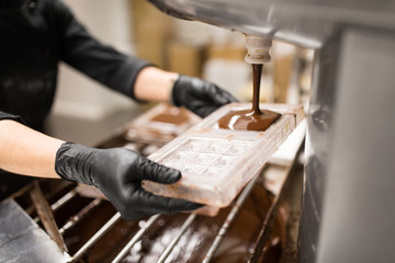 production, cooking and people concept - confectioner filling candy mold with chocolate at...