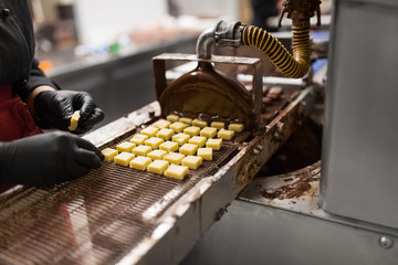 production, candy shop and people concept - confectioner setting candies to chocolate coating...