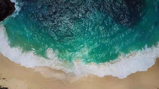 Beach scene, view from above - waves of turquoise ocean waters crashing on stones. Kelingking beach, Nusa Penida. 4k footage.