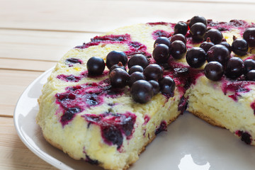 Baked round black currant cake on white plate on light wooden background. Shallow focus. Soft light